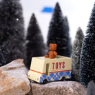 Toy truck with a teddy bear on top in a snowy landscape with trees and rocks.
