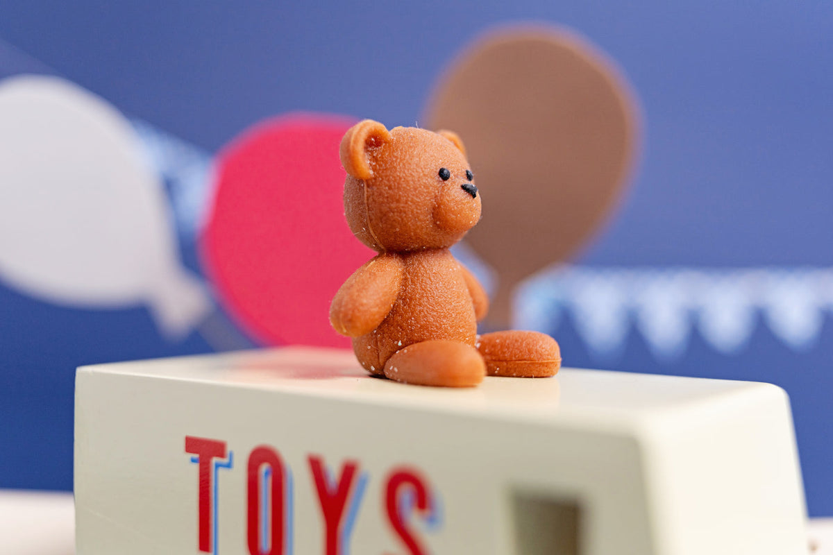 Small brown teddy bear on a block with 'TOYS' letters against a blue background