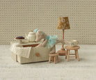Miniature tea set with teddy bear and lamp in a room with patterned wallpaper.