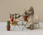 Stuffed rabbit in a floral dress tending to plants in a miniature room setting.