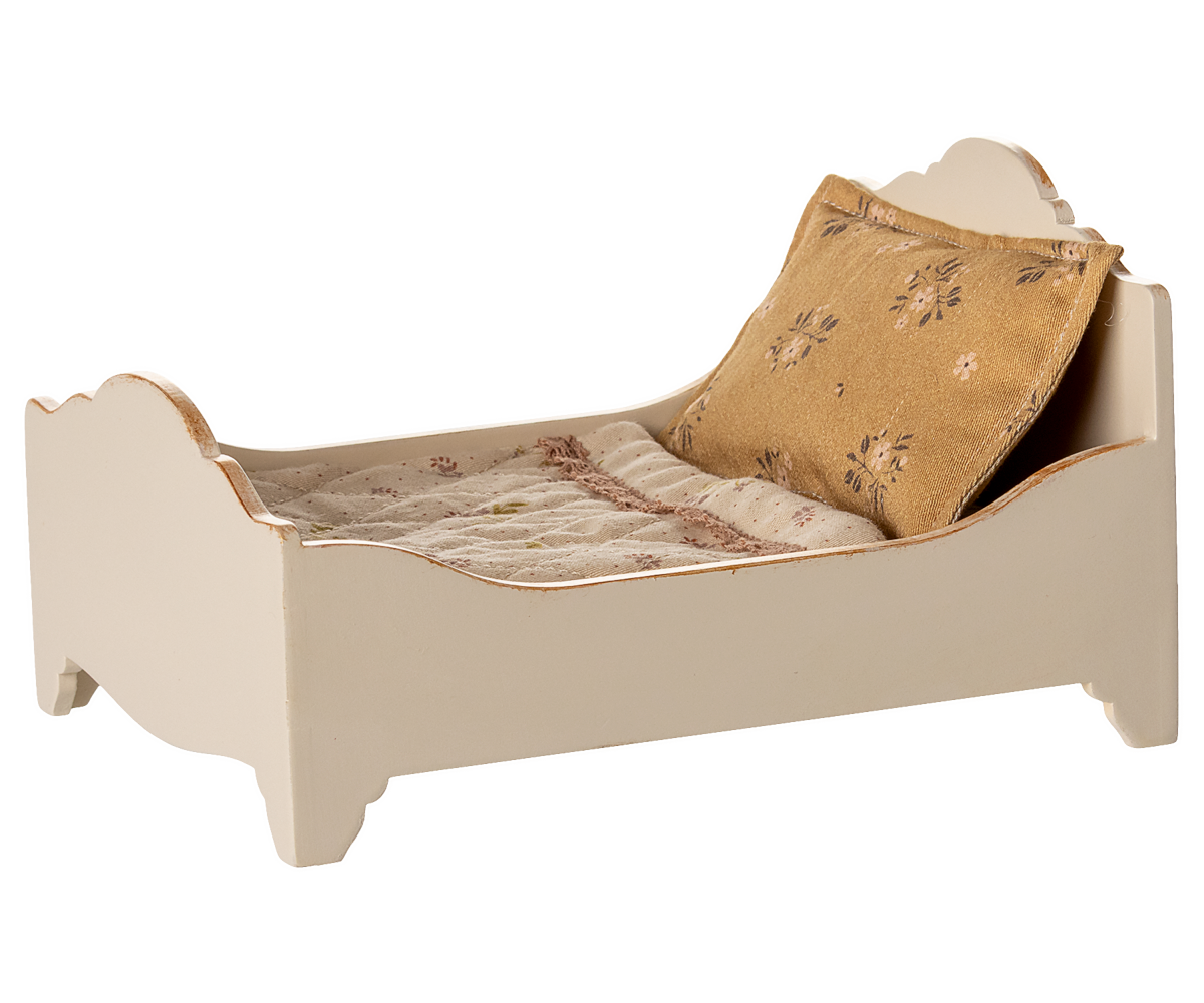 Small bed with beige bedding and a decorative pillow on a white background