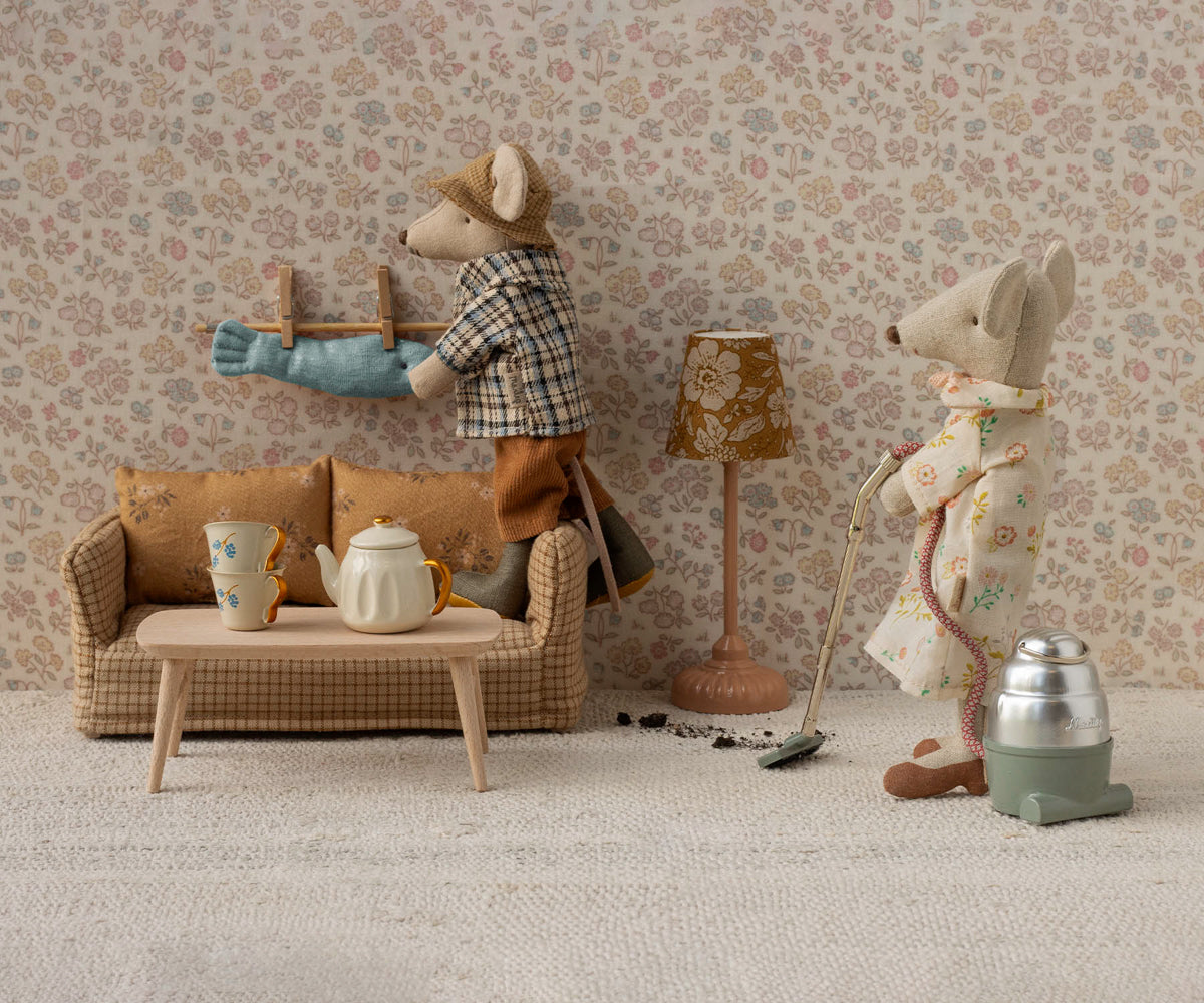 Miniature living room scene with toy mice and furniture against a floral wallpapered wall.