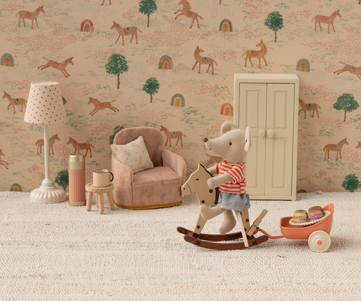 Children's room with toys, chair, and lamp against a wallpapered wall with animal patterns.