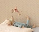 Stuffed animal lying on a bed with another animal hanging above, against a patterned wall.