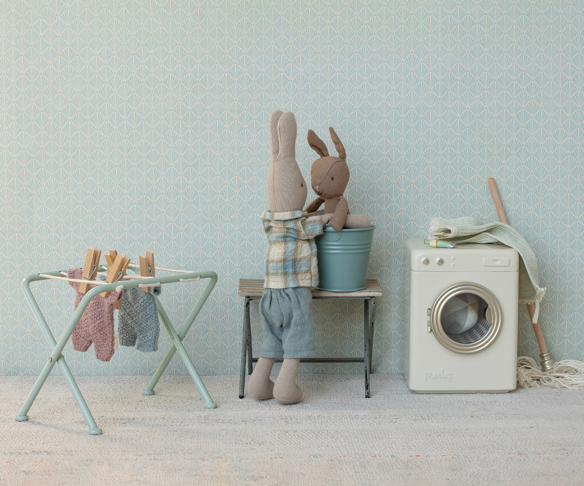 Children's room with stuffed animals, washing machine, and drying rack against a light blue wall.