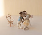 Two stuffed animal dolls in ballet costumes standing next to a small chair on a light background