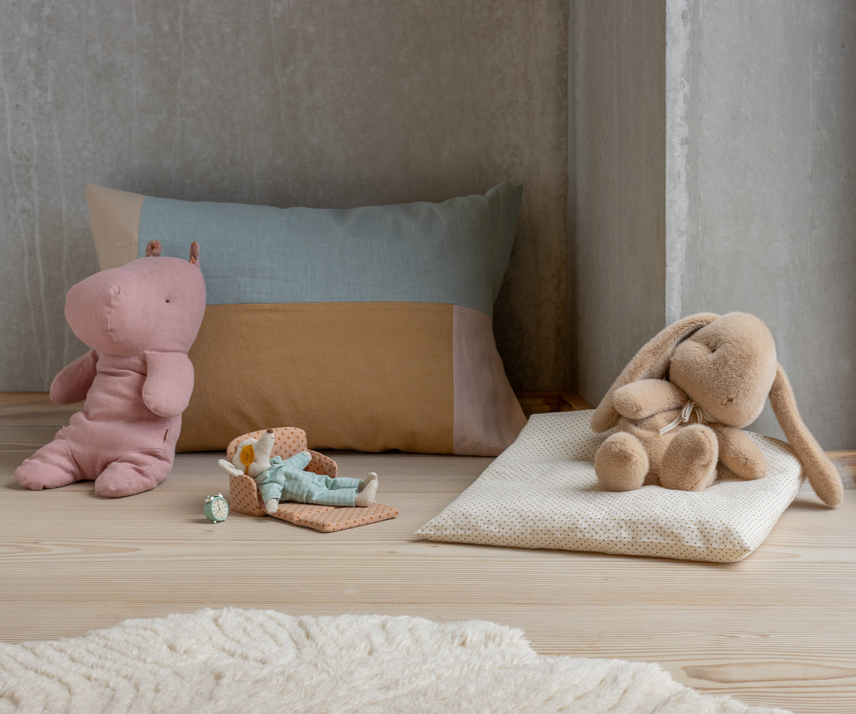 Children's toys including a pink hippo, brown bunny, and green teddy bear on a wooden surface with pillows in the background.
