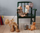 Toy bear on a leash with other teddy bears and accessories on a chair against a gray wall.