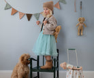 Child standing on a chair in a room with toys and a dog.