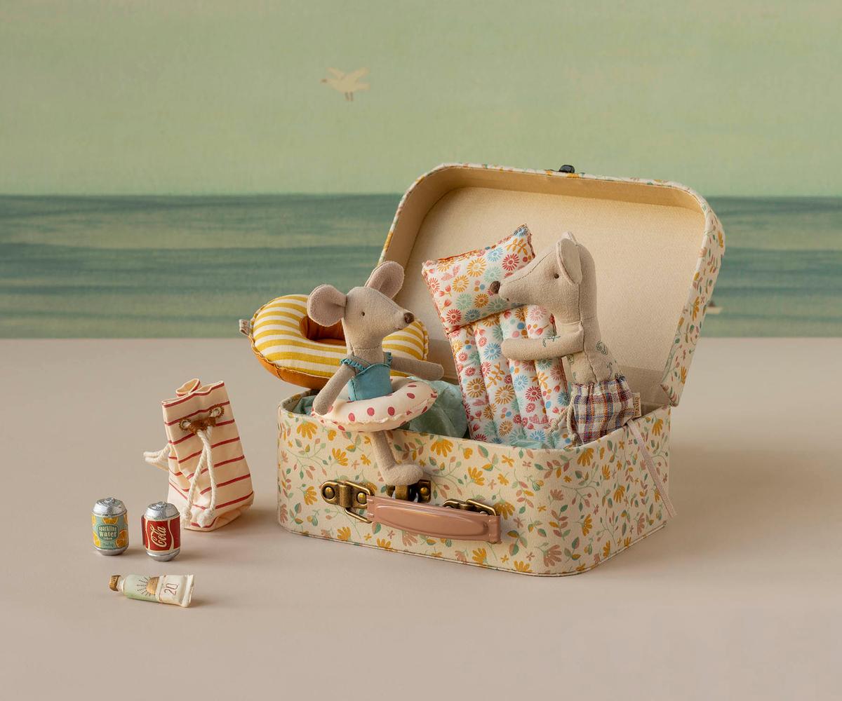 Toy mice in a suitcase with travel accessories on a neutral background