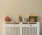 Decorative shelf with small figurines and toys on a white radiator against a beige wall.