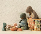 Children's toys, including a dinosaur and teddy bear, in a basket against a floral-patterned wall.