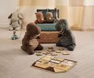 Stuffed animal toys playing with a suitcase and cards on a wooden floor.