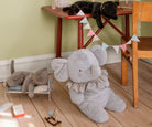 Gray elephant plush toy on a wooden floor with a child's play area in the background.