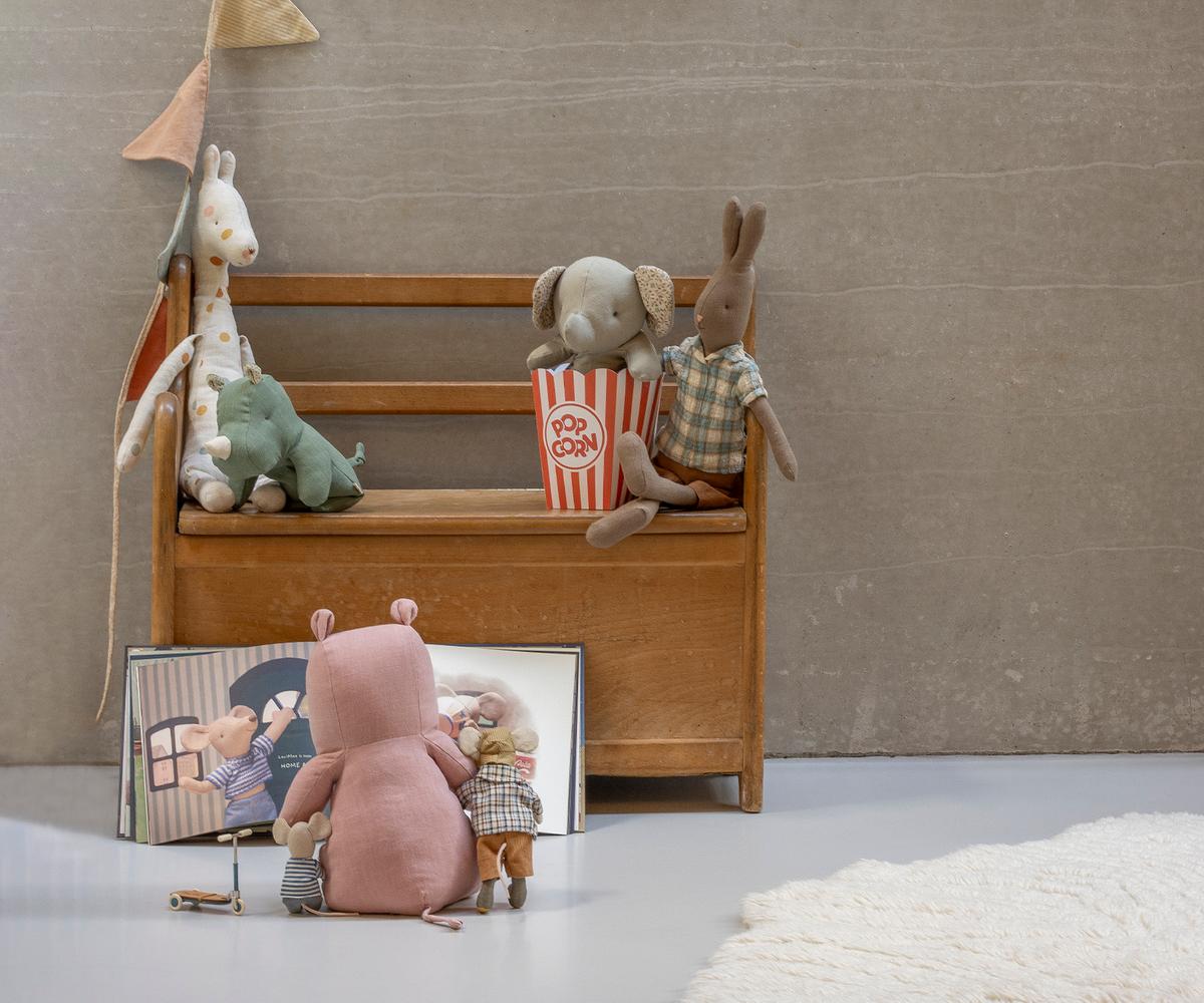 Stuffed animals on a small wooden bench with a mirror, popcorn, and a flag in a minimalistic setting.