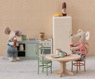 Miniature kitchen scene with toy mice, refrigerator, and furniture against a patterned wall.