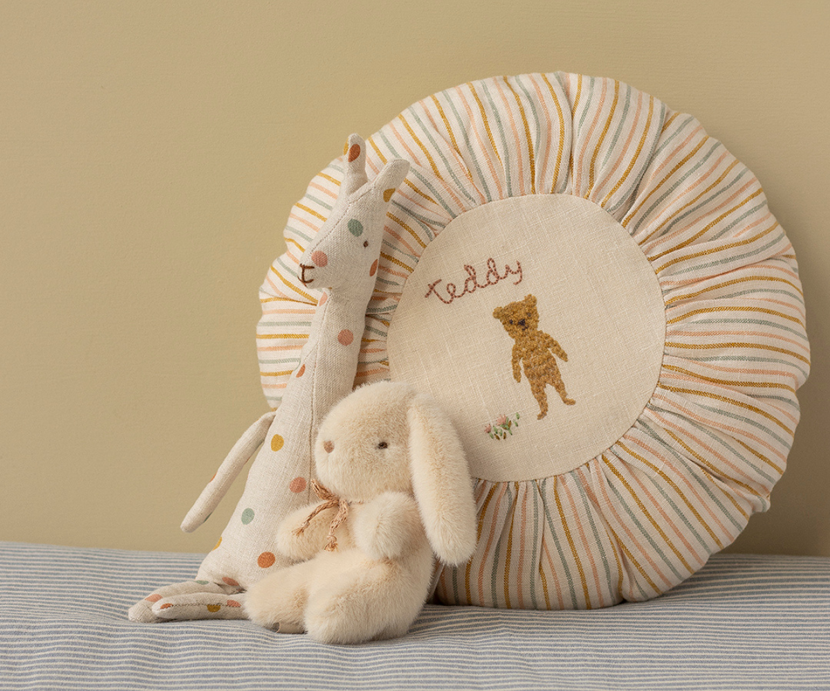 Round cushion with teddy bear design, accompanied by stuffed animals on a striped surface.