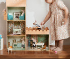 Child playing with a dollhouse filled with miniature furniture and accessories.