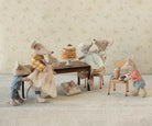 Stuffed animal family gathered around a small table with a cake, set against a floral wallpaper background.