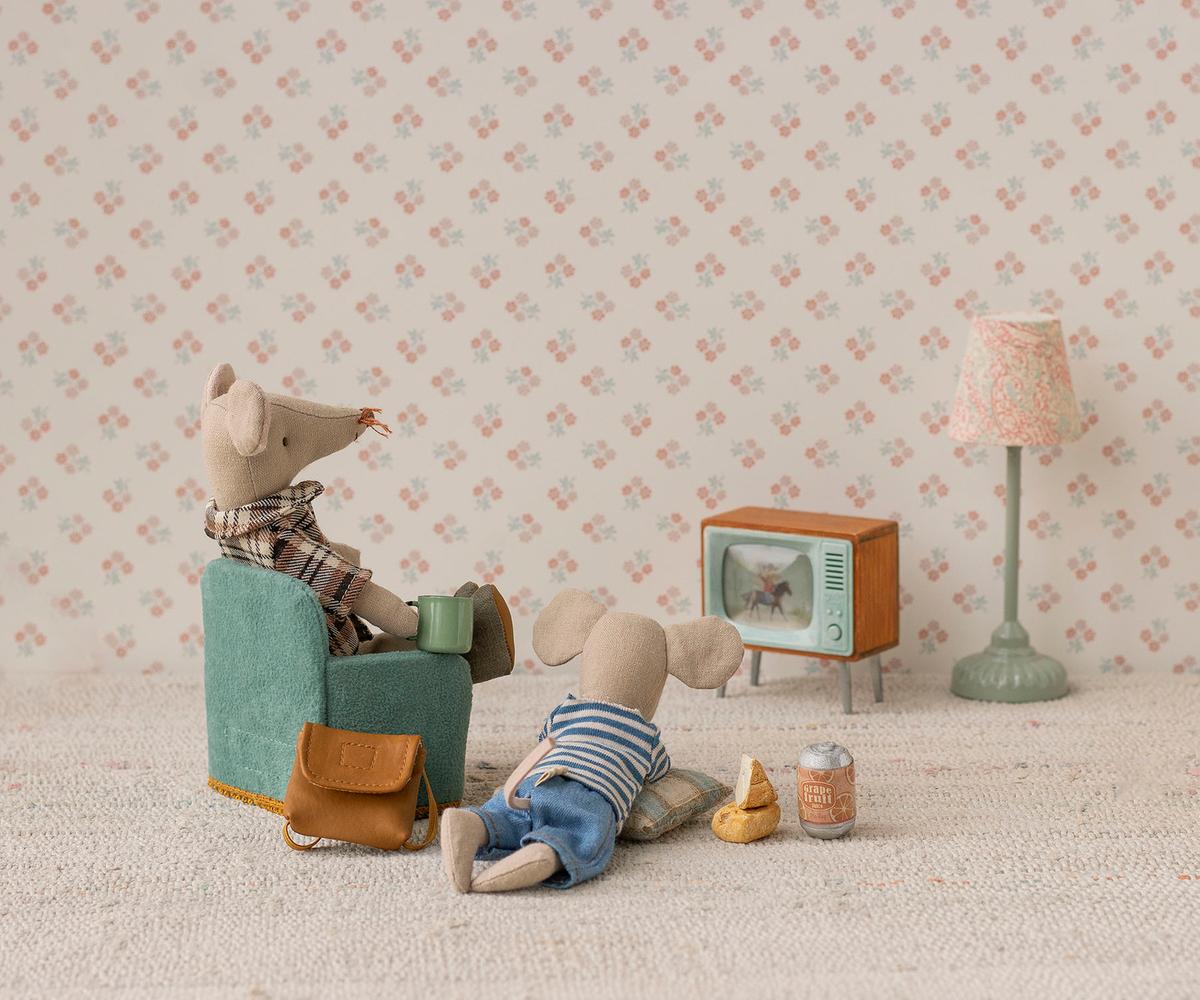 Two toy mice in a room with a small TV and lamp on a patterned wallpaper background.