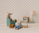 Two toy mice in a room with a small TV and lamp on a patterned wallpaper background.
