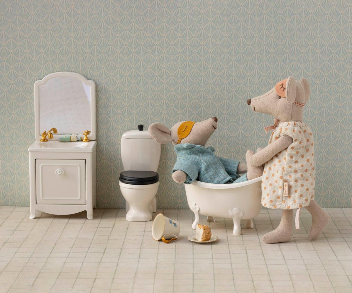 Maileg Mum mouse standing beside a miniature bathtub where Dad mouse sits inside, set in a dollhouse bathroom with a small toilet, sink, and tiled floor.