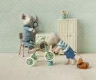 Two toy mice with a tricycle and other items in a room with light blue walls and a white floor.