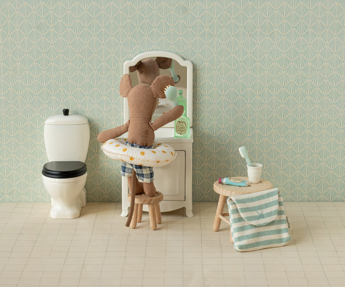 Stuffed teddy bear in a bathtub with a stool and towel in a bathroom setting