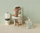 Stuffed teddy bear in a bathtub with a stool and towel in a bathroom setting