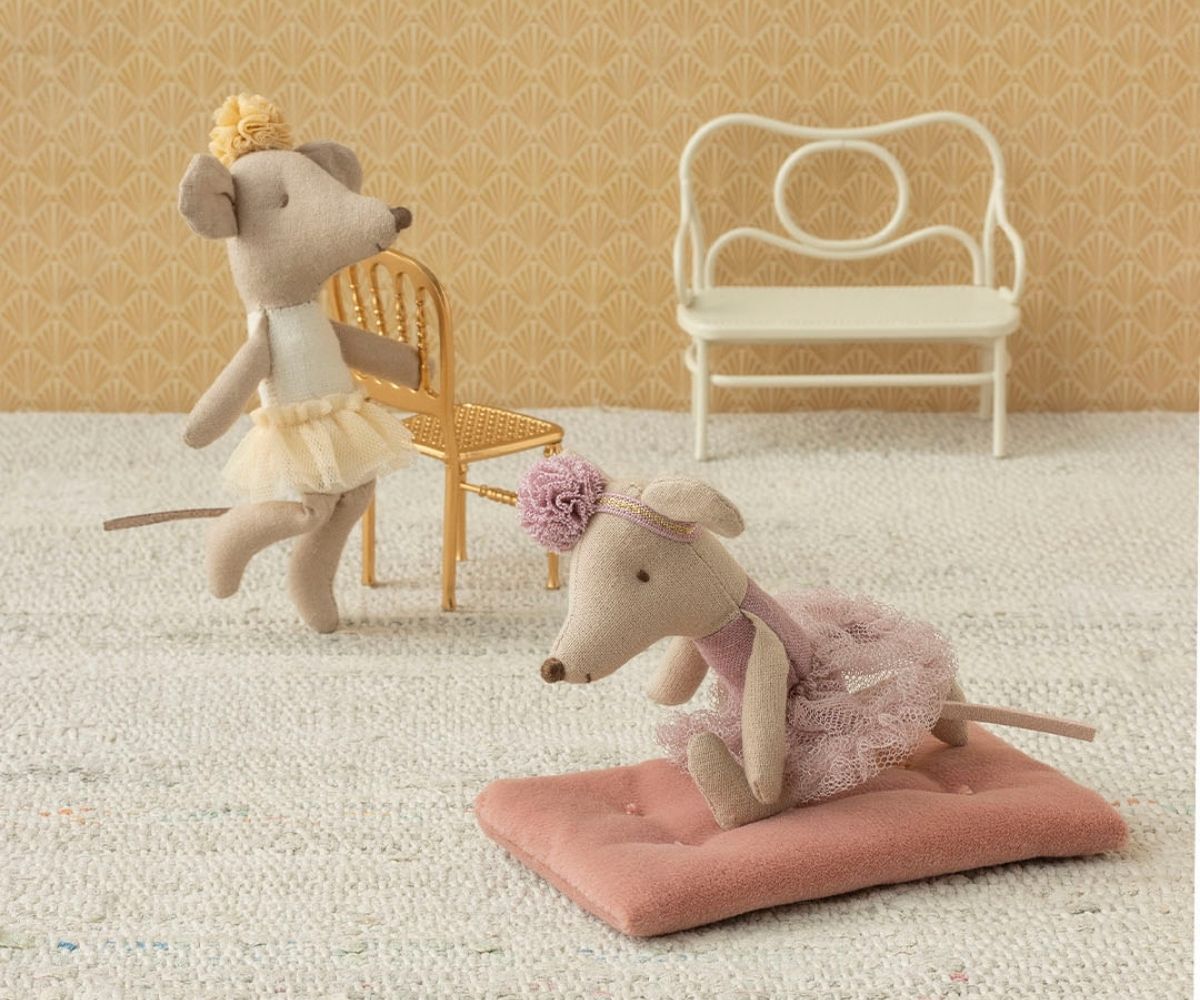 Two plush mouse toys in decorative outfits on a textured surface with chairs in the background.