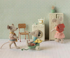 Three toy mice in a room with a chair, washing machine, and cabinet.