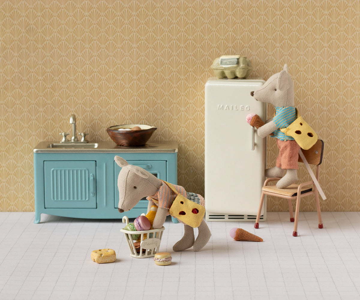 Toy kitchen set with a refrigerator, sink, and chairs with toy figures on a patterned wall background.