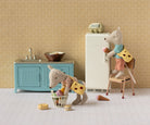 Toy kitchen set with a refrigerator, sink, and chairs with toy figures on a patterned wall background.