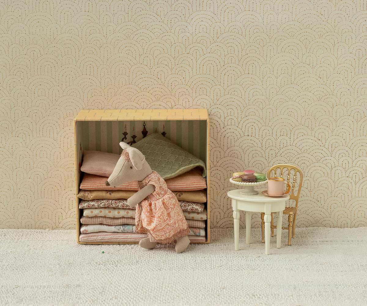 A Maileg toy set featuring a Big Sister mouse standing next to a wooden bed frame piled high with colorful layered mattresses, with a miniature table and chair set nearby holding tiny treats and a teapot.