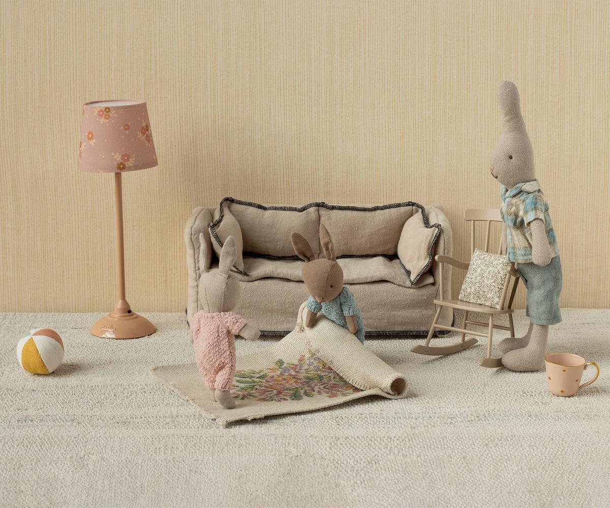 Children's room with toy sofa, rabbit figure, and lamp against a beige wall.