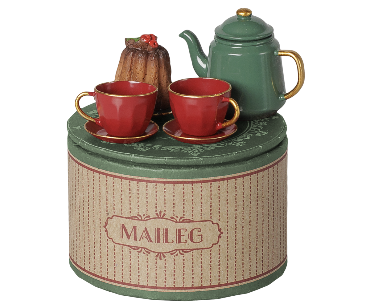 A Maileg Christmas tea party set featuring a round decorative gift tin, a green metal teapot with a gold knob and handle, two red teacups and saucers, and a miniature cake on a scalloped plate.