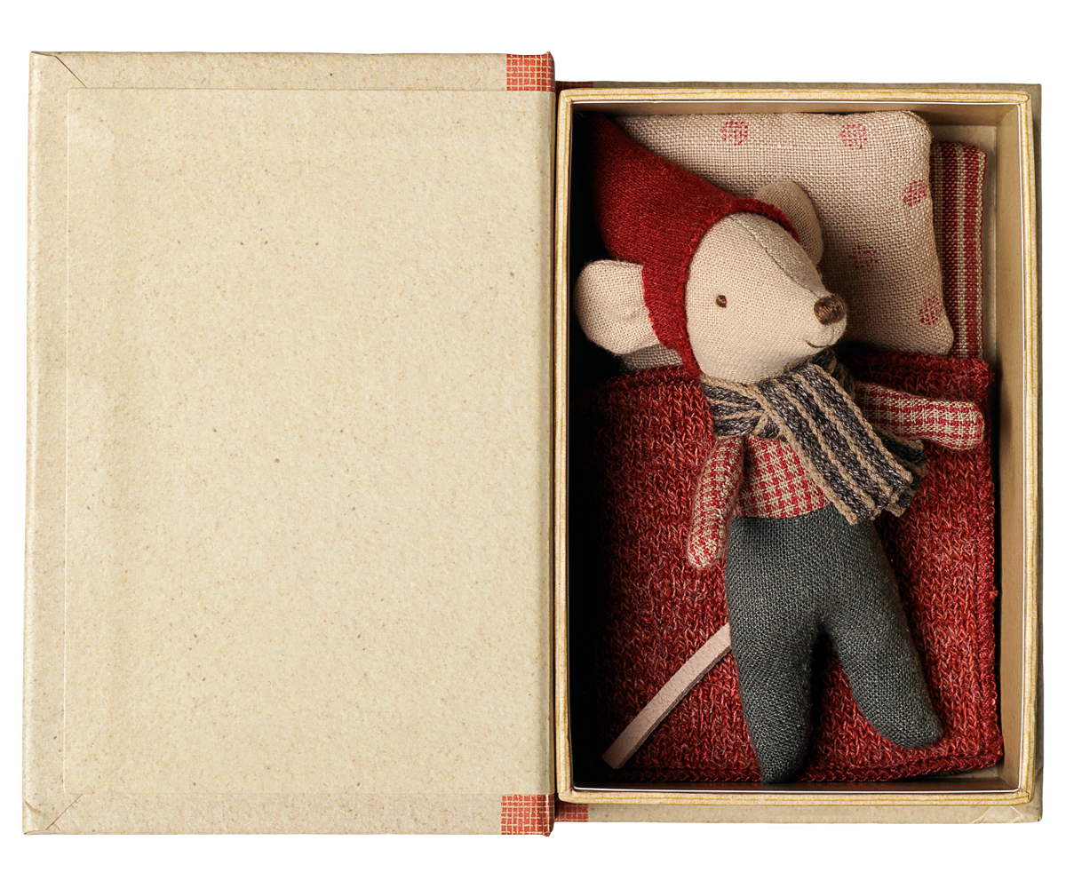 A small plush mouse toy dressed in a red hat and scarf with gray pants, displayed inside an open beige gift box with a red patterned pillow.
