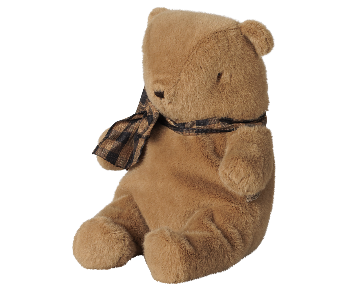 A small brown plush teddy bear by Maileg sitting upright against a transparent background, wearing a brown and black plaid bow around its neck.