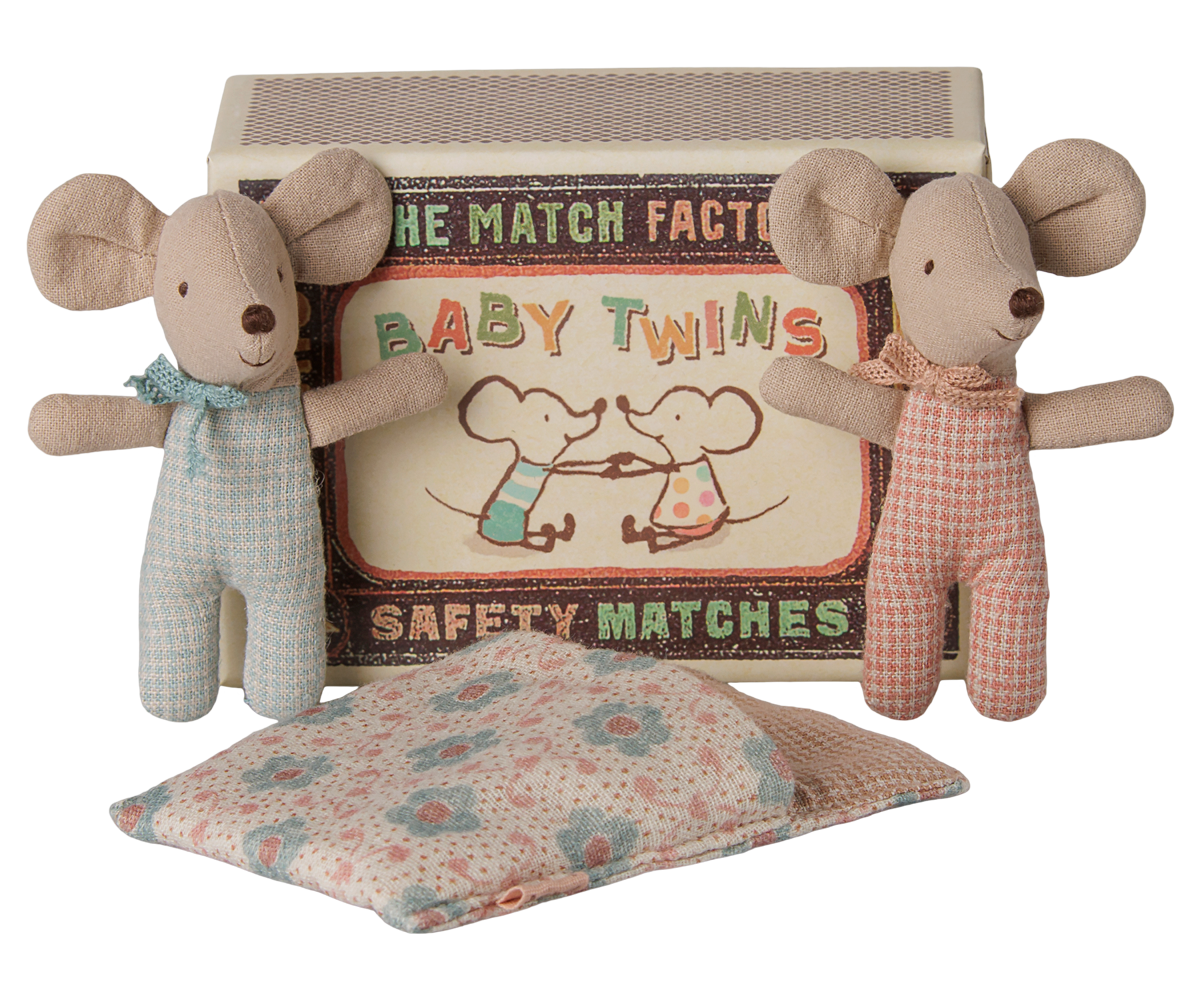 Two Maileg baby mice toys standing upright on either side of an open matchbox labeled "Baby Twins Safety Matches," with a patterned quilted sleeping bag resting in front.
