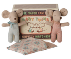 Two Maileg baby mice toys standing upright on either side of an open matchbox labeled "Baby Twins Safety Matches," with a patterned quilted sleeping bag resting in front.