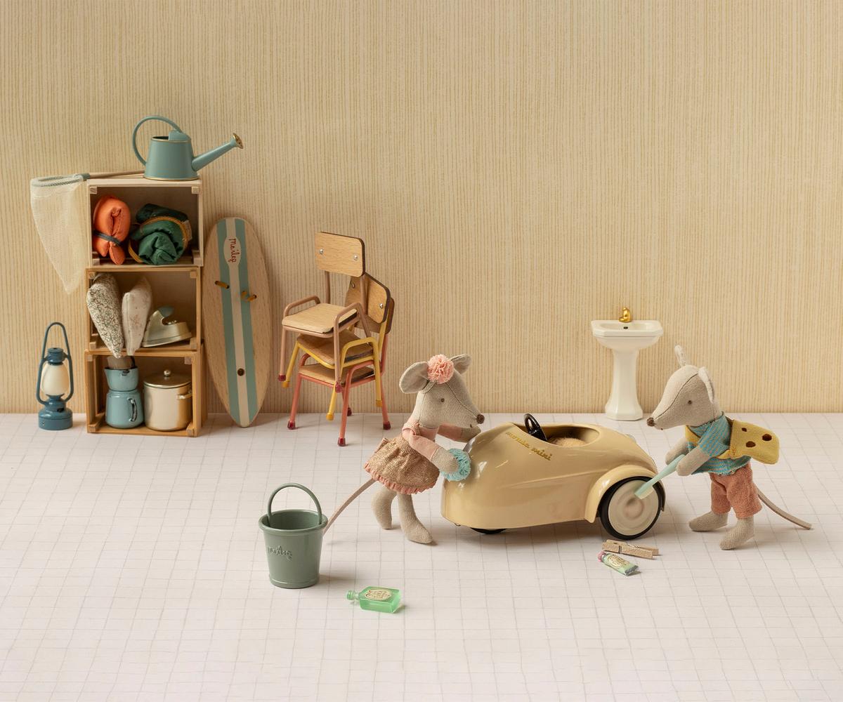 A styled miniature scene with small animal figurines and toy props arranged on a white floor against a beige wall.