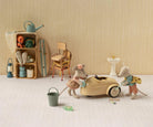 A styled miniature scene with small animal figurines and toy props arranged on a white floor against a beige wall.