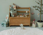 A wooden toy bench styled with wrapped gift boxes, small decorative items, and a plush mouse in a cozy nursery setting against a sage green wall.
