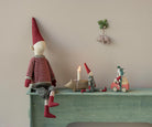 A festive holiday display featuring a large Maileg mouse doll in a red and white striped sweater and a tall pixy hat seated on a mint green ledge, with smaller Maileg mice, a miniature car-shaped box, and a toy pig figurine arranged nearby in front of a warm-toned background.