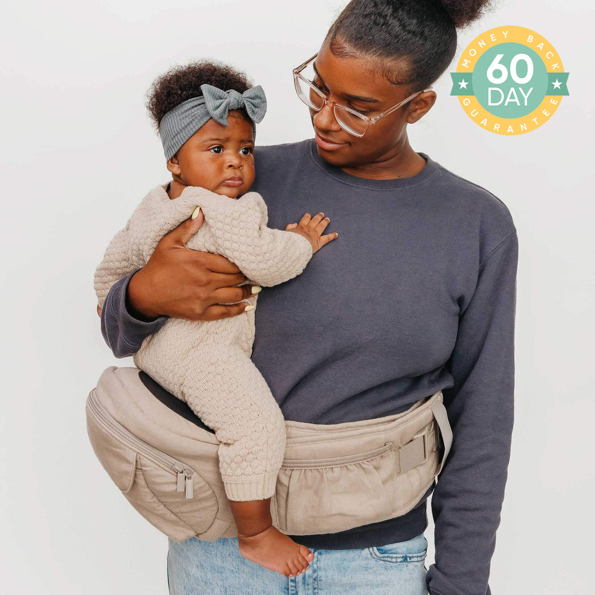 Woman holding a baby in a carrier with a neutral background