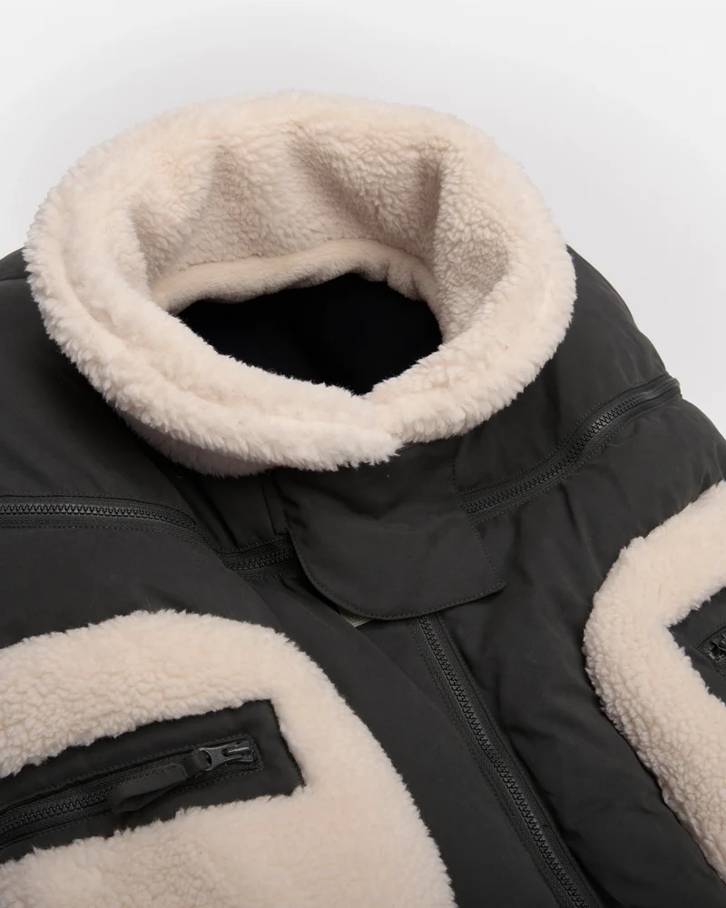 Benji Applique Car Seat Cocoon by 7AM Enfant featuring a closeup of the dark grey weatherproof outer shell, plush ivory sherpa fleece trim around the collar and zippered side pocket, and front zipper detail.