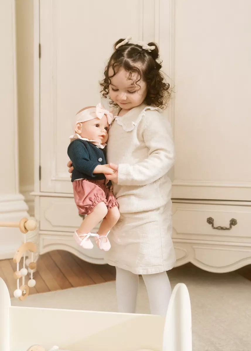 Child holding a doll in a room with white furniture