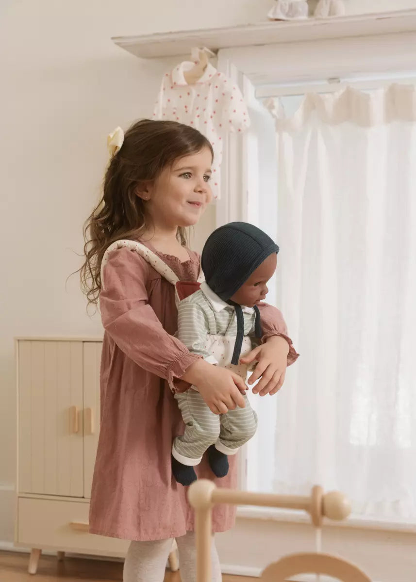Young girl holding a doll in a room with light-colored walls and furniture.