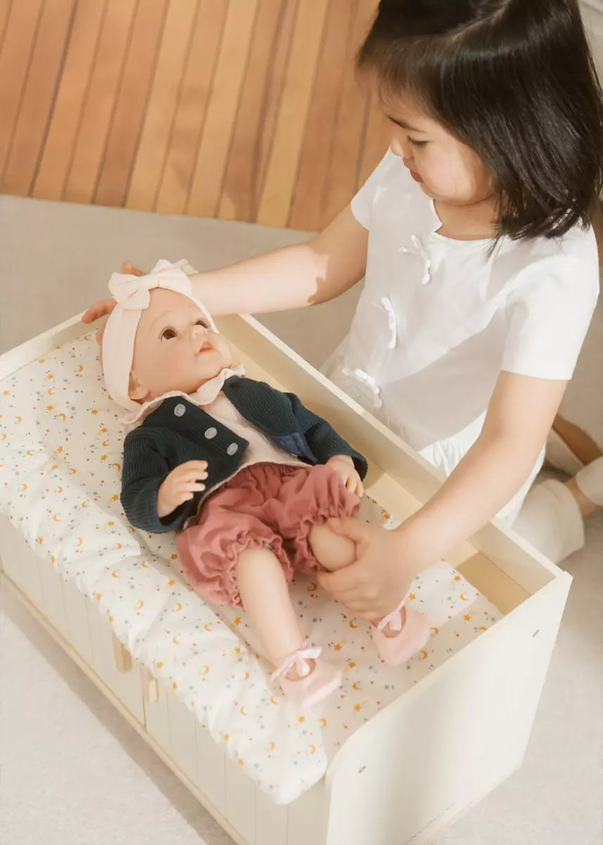 Child playing with a baby doll on a changing table.