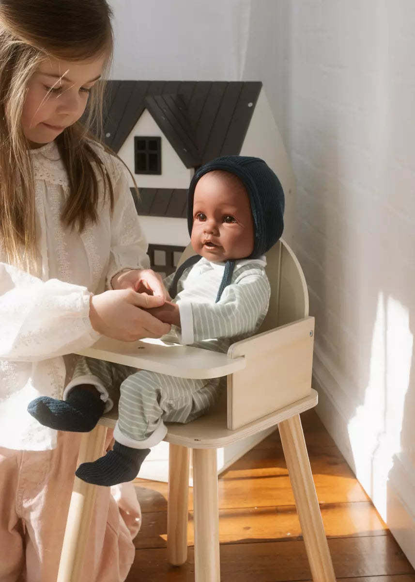 Two children playing with a baby doll in a room with a white wall and wooden floor.